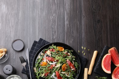 Photo of Tasty salad with arugula, cheese, grapefruit, vegetable and balsamic sauce served on dark wooden table, flat lay. Space for text