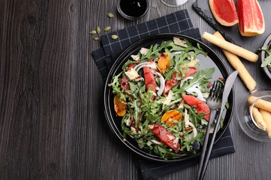 Photo of Tasty salad with arugula, cheese, grapefruit, vegetable and balsamic sauce served on dark wooden table, flat lay. Space for text
