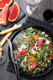 Photo of Tasty salad with arugula, cheese, grapefruit, vegetable and balsamic sauce served on dark wooden table, flat lay