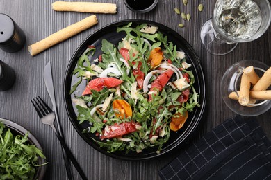 Photo of Tasty salad with arugula, cheese, grapefruit, vegetable and balsamic sauce served on dark wooden table, flat lay