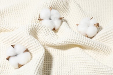 Photo of Clean waffle towel and cotton flowers as background, top view