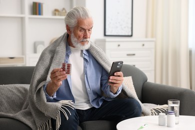 Photo of Senior man with pills having online consultation with doctor via smartphone at home
