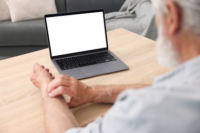 Photo of Senior man having online consultation with doctor via laptop at table indoors, closeup