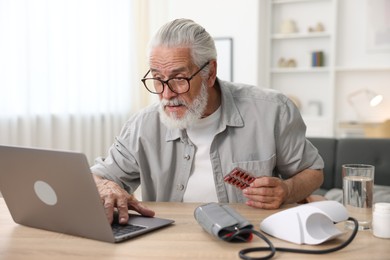 Photo of Senior man with pills having online consultation with doctor via laptop at table indoors