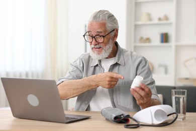 Photo of Senior man with pills having online consultation with doctor via laptop at table indoors