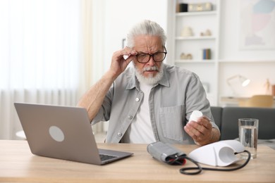Photo of Senior man with pills having online consultation with doctor via laptop at table indoors