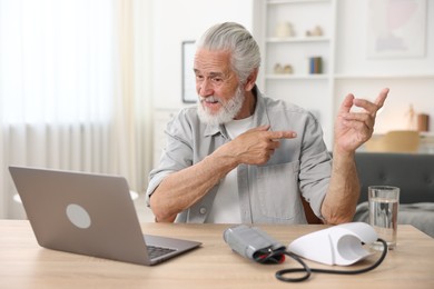 Photo of Senior man having online consultation with doctor via laptop at table indoors