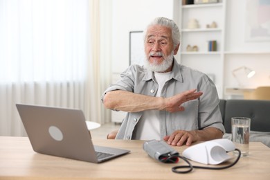 Photo of Senior man having online consultation with doctor via laptop at table indoors