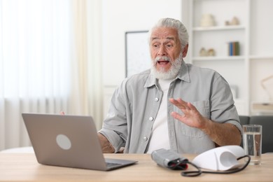 Photo of Senior man having online consultation with doctor via laptop at table indoors