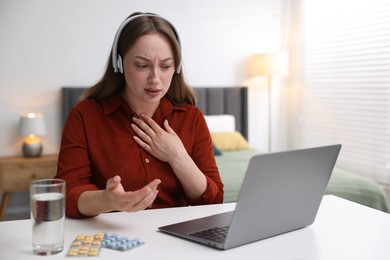 Photo of Woman in headphones having online consultation with doctor via laptop at table indoors