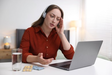 Photo of Woman in headphones having online consultation with doctor via laptop at table indoors