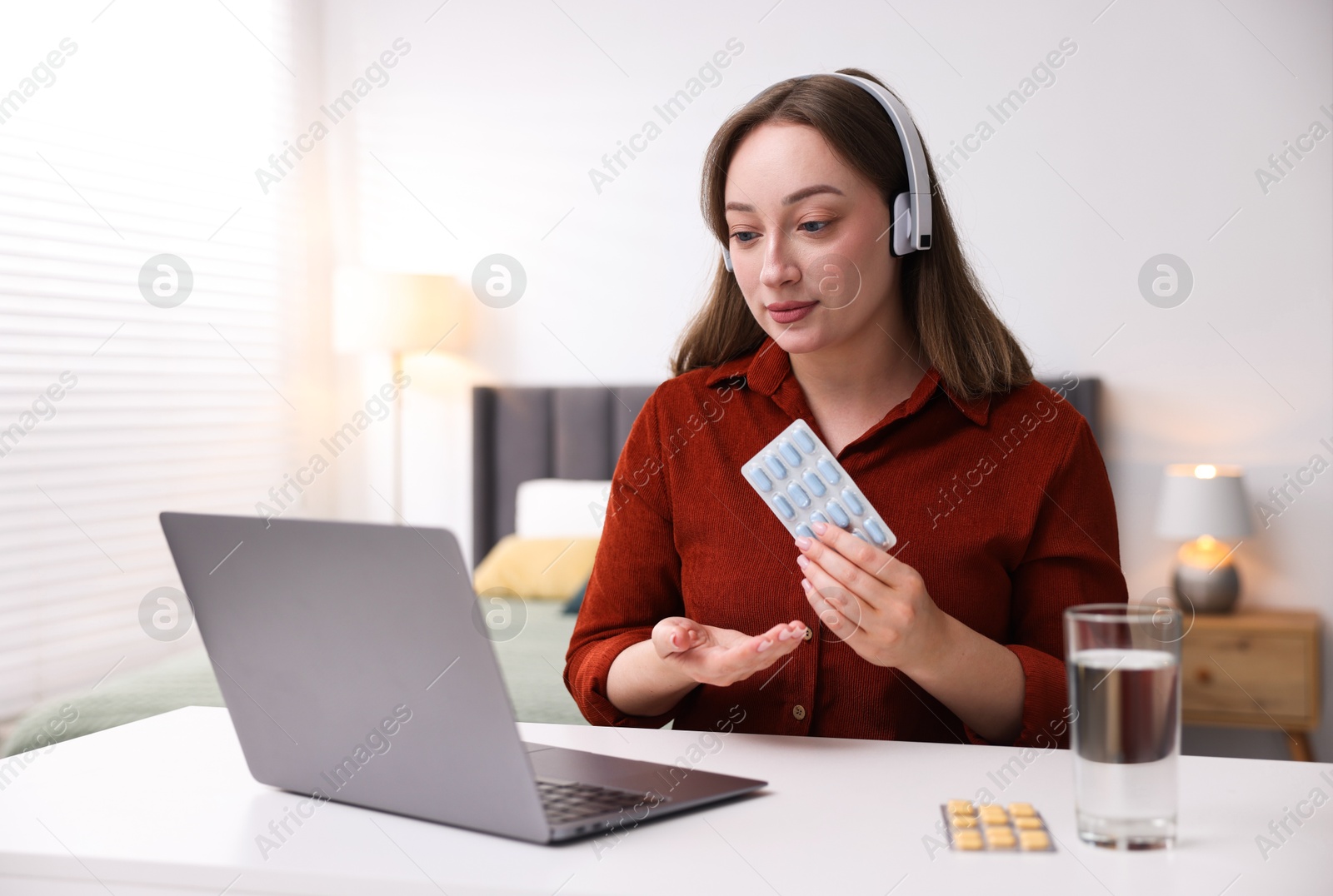 Woman in headphones with pills having online consultation with doctor via laptop at table indoors Photo of Woman in headphones with pills having online consultation with doctor via laptop at table indoors