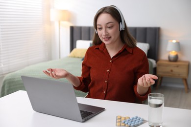 Photo of Woman in headphones having online consultation with doctor via laptop at table indoors