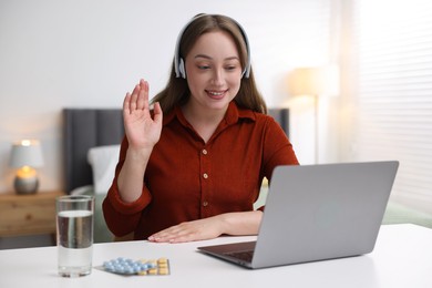 Photo of Woman in headphones having online consultation with doctor via laptop at table indoors