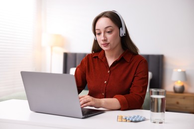 Photo of Woman in headphones having online consultation with doctor via laptop at table indoors
