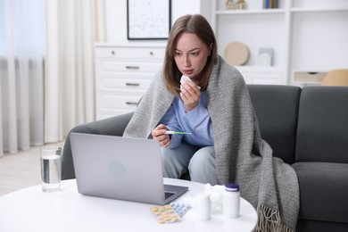 Photo of Sick woman with thermometer and paper tissue having online consultation with doctor via laptop at home