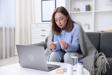 Photo of Sick woman with thermometer having online consultation with doctor via laptop at home