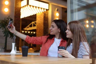 Photo of Mother and her teenage daughter taking selfie at table in cafe