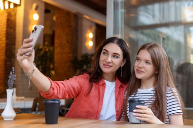 Photo of Mother and her teenage daughter taking selfie at table in cafe
