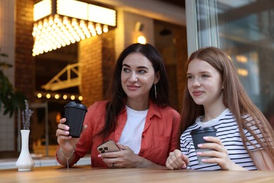 Photo of Mother and her teenage daughter drinking coffee at table in cafe