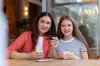 Photo of Mother and her teenage daughter drinking coffee at table in cafe
