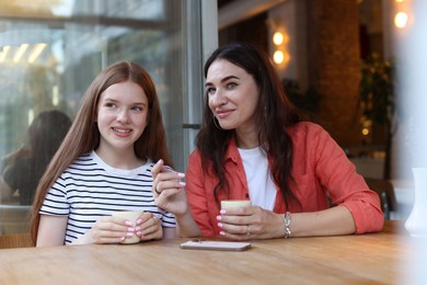 Photo of Mother and her teenage daughter drinking coffee at table in cafe