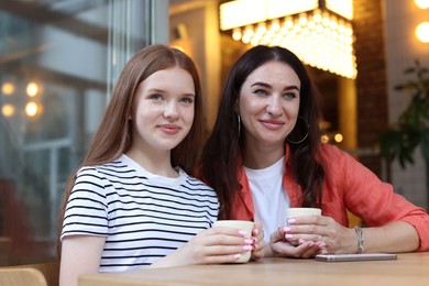 Photo of Mother and her teenage daughter drinking coffee at table in cafe