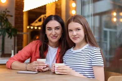 Photo of Mother and her teenage daughter drinking coffee at table in cafe