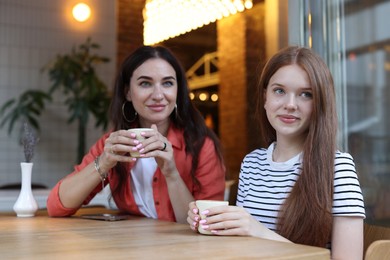 Photo of Mother and her teenage daughter drinking coffee at table in cafe