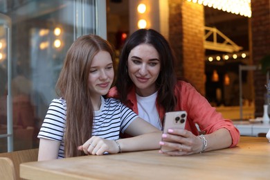 Photo of Mother and her teenage daughter using smartphone at table in cafe