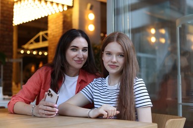 Photo of Mother and her teenage daughter with smartphone at table in cafe