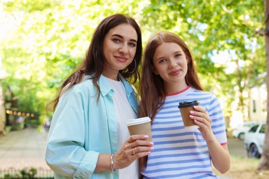 Photo of Portrait of beautiful mother and her teenage daughter with paper cups on city street