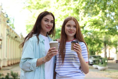 Photo of Portrait of beautiful mother and her teenage daughter with paper cups on city street