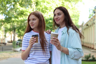 Photo of Beautiful mother and her teenage daughter with paper cups on city street
