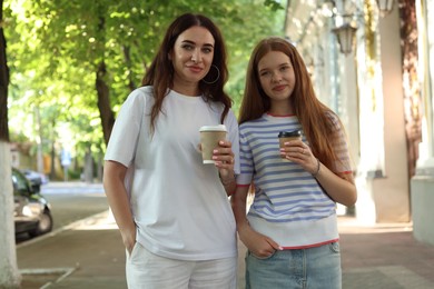 Photo of Portrait of beautiful mother and her teenage daughter with paper cups on city street