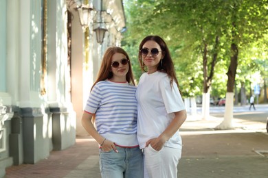 Photo of Portrait of beautiful mother and her teenage daughter in sunglasses on city street