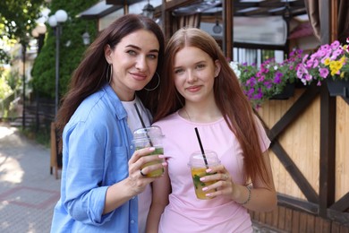 Photo of Portrait of beautiful mother and her teenage daughter with refreshing drinks on city street