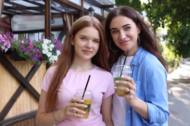 Photo of Portrait of beautiful mother and her teenage daughter with refreshing drinks on city street