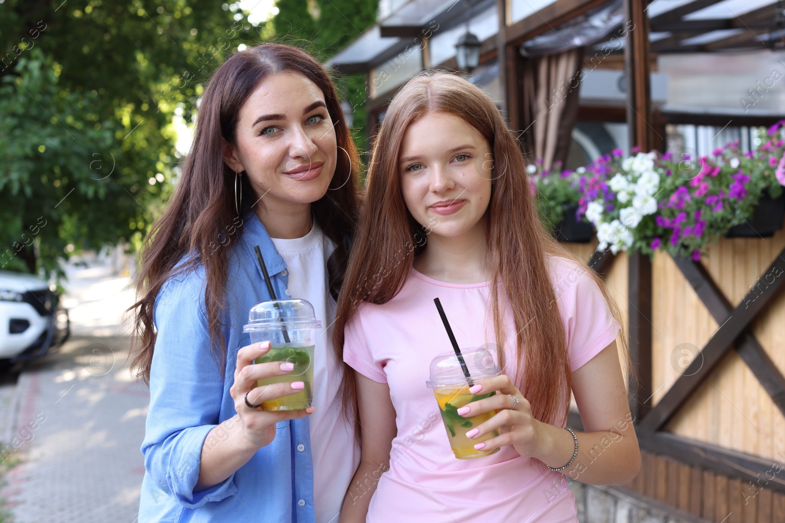 Photo of Portrait of beautiful mother and her teenage daughter with refreshing drinks on city street