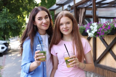 Photo of Portrait of beautiful mother and her teenage daughter with refreshing drinks on city street