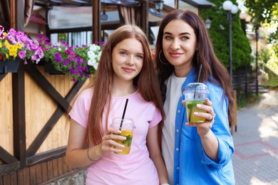 Photo of Portrait of beautiful mother and her teenage daughter with refreshing drinks on city street