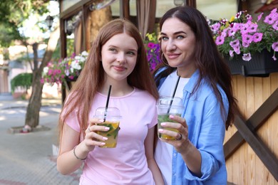 Photo of Portrait of beautiful mother and her teenage daughter with refreshing drinks on city street