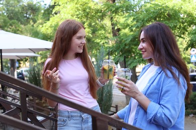 Photo of Beautiful mother and her teenage daughter with refreshing drinks talking on stairs outdoors