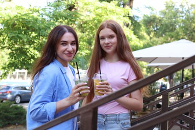 Photo of Portrait of beautiful mother and her teenage daughter with refreshing drinks on stairs outdoors