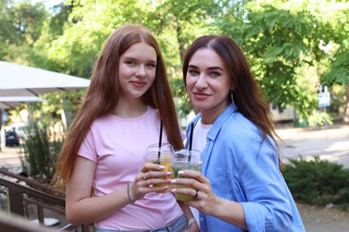 Photo of Portrait of beautiful mother and her teenage daughter with refreshing drinks on city street