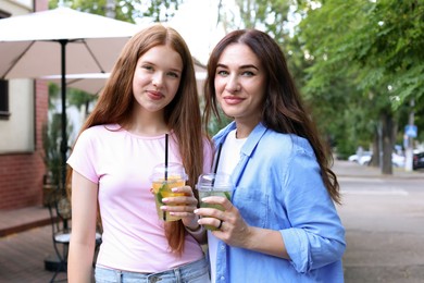 Photo of Portrait of beautiful mother and her teenage daughter with refreshing drinks on city street