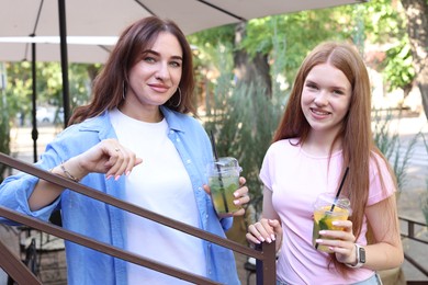 Photo of Portrait of beautiful mother and her teenage daughter with refreshing drinks outdoors