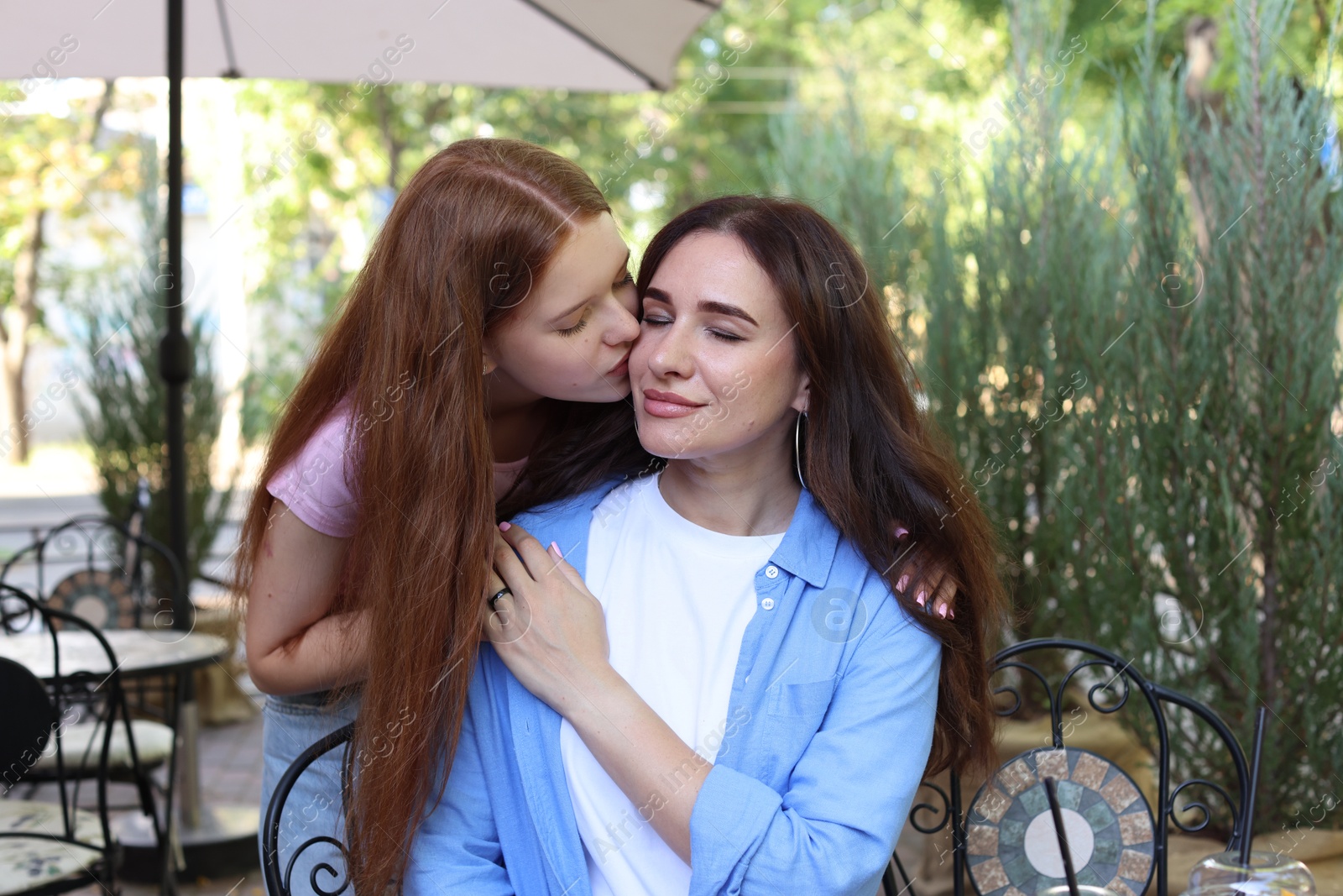 Teenage daughter kissing her mother in outdoor cafe Photo of Teenage daughter kissing her mother in outdoor cafe