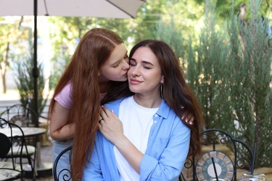 Photo of Teenage daughter kissing her mother in outdoor cafe