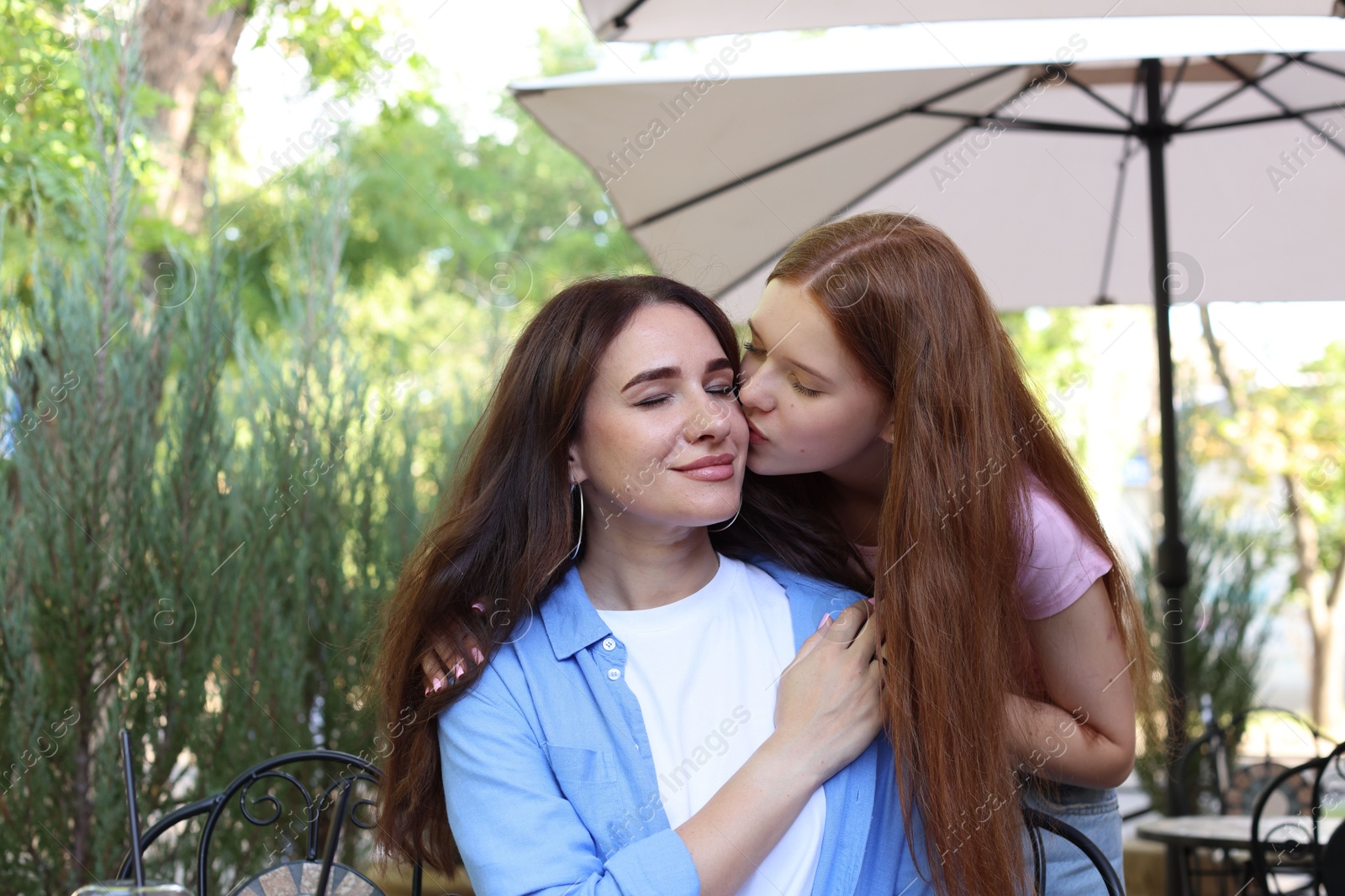 Photo of Teenage daughter kissing her mother in outdoor cafe
